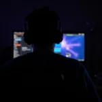 Gamer wearing headphones in a dark room lit by a monitor