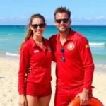 Couples in matching red lifeguard costumes posing on a sunny beach.